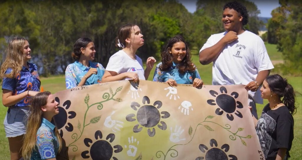 A group of smiling young people standing outdoors in a grassy area