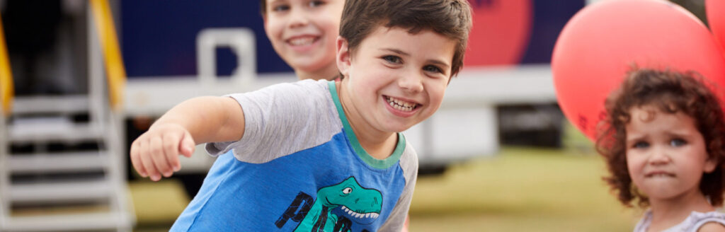 Three young children smiling and playing outdoors during a community event
