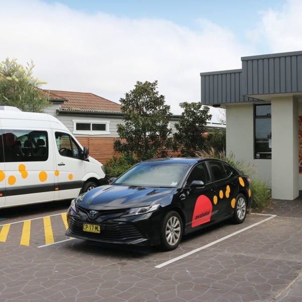A black sedan and a white van, both featuring orange "Awabakal" branding and dot art