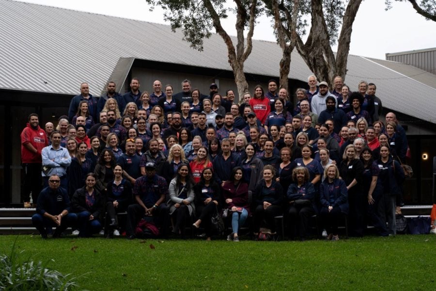 A large group of staff members, many wearing navy blue shirts with indigenous-themed patterns